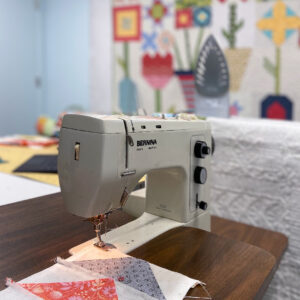 Sewing machine with design wall and ironing board in the background.
