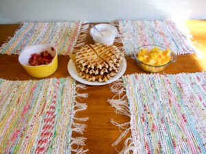 Fabric placemats on a table with waffles and fruit.
