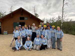 Young women in front of a log cabin in the woods.
