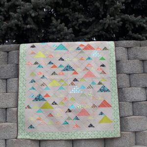Scrappy half square triangle quilt set on point to make a mountain range hanging on a retaining wall
