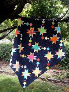 Scrappy shooting star quilt hanging in a tree