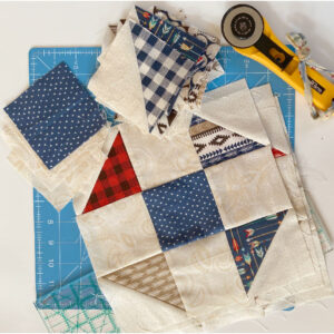 Scrappy shoofly block with rotary cutter, cutting mat and extra fabric pieces.