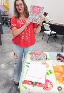 Scrap Quilts book held by author with a display table of some of the projects