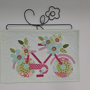 Appliqued bicycle mini quilt with flowers on a metal hanging rod