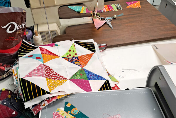Bernina sewing machine with cut triangles ready to sew and a stack of quilt blocks.