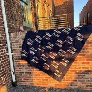 Scrappy half square triangle quilt with black background on a brick wall.