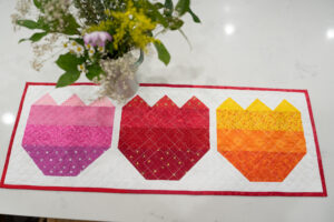 springtime quilted table runner with vase of flowers.