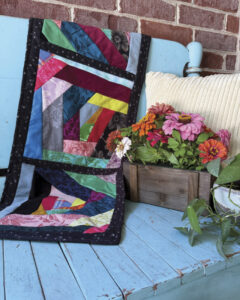crazy quilt table runner draped over bench with basket of flowers.