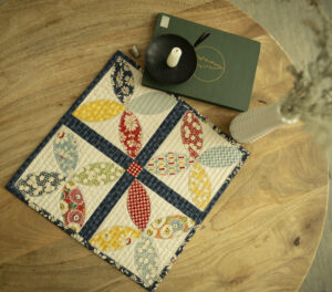 Small table topped with a quilted table topper book candle and vase of flowers.